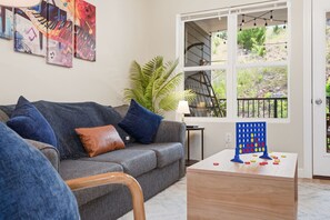 A living room with a grey sofa, a coffee table, a plant, and a window with a view of greenery.