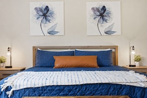 A bedroom with a bed, two nightstands, a wooden headboard, and two wall-mounted flower paintings.