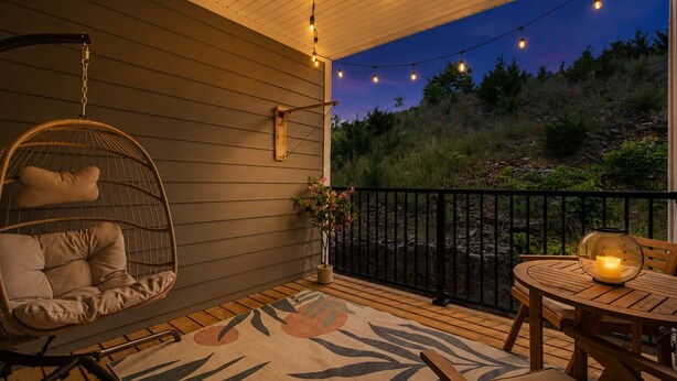 A wooden deck with a hanging chair, a table with a candle, and a view of the outdoors.