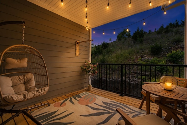 A wooden deck with a hanging chair, a table with a candle, and a view of the outdoors.