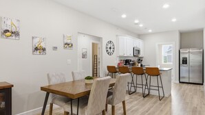 A modern kitchen with white cabinets, a stainless steel refrigerator, and a dining area with a wooden table and chairs.