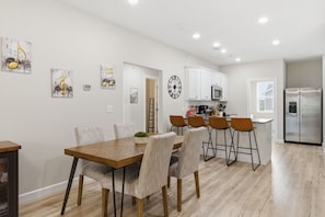 A modern kitchen with white cabinets, a stainless steel refrigerator, and a dining area with a wooden table and chairs.