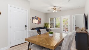 A dining area with a wooden table, grey upholstered chairs, a ceiling fan, and a view through glass doors to an outdoor patio.