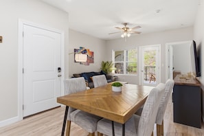 A dining area with a wooden table, grey upholstered chairs, a ceiling fan, and a view through glass doors to an outdoor patio.