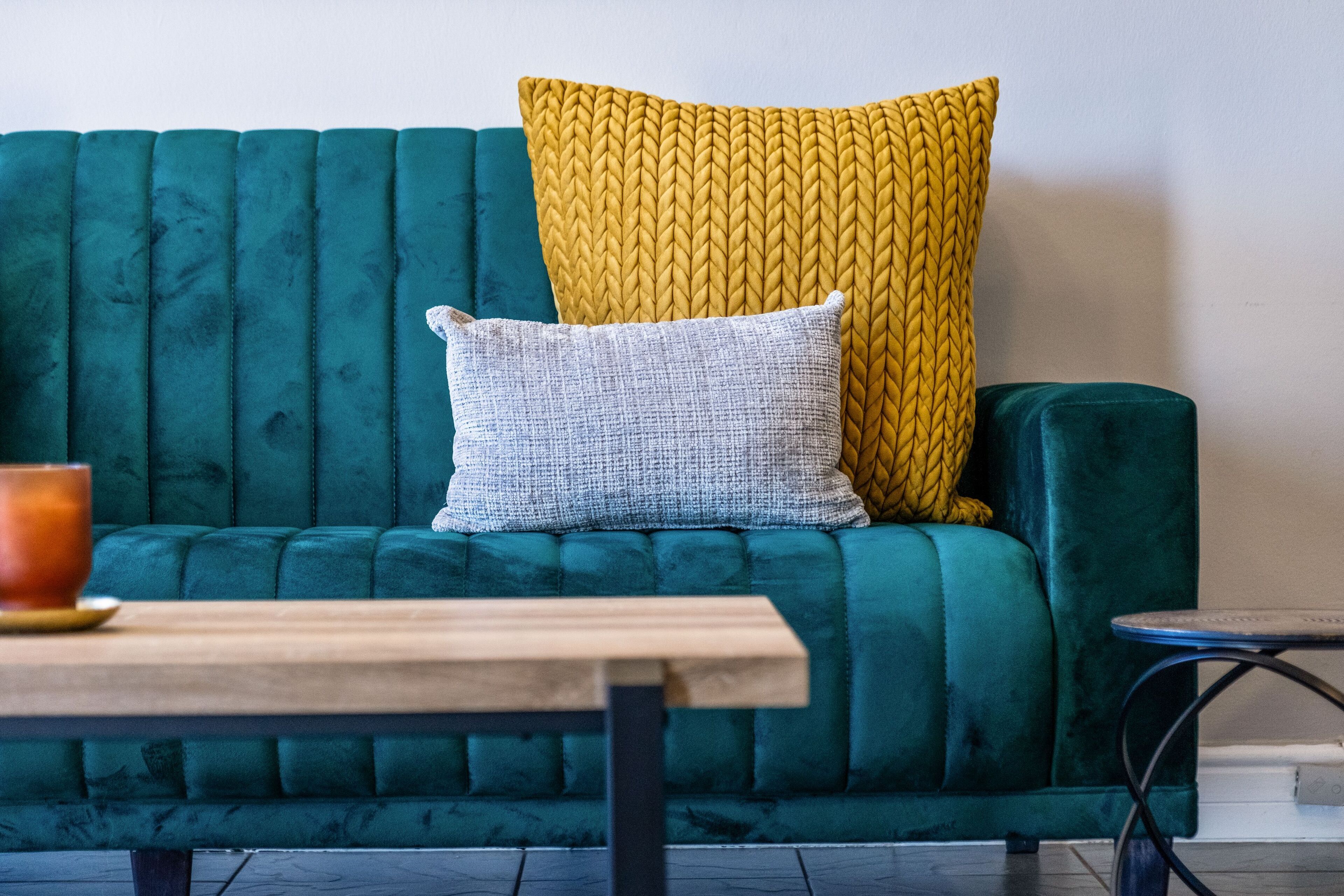 Un sofá color esmeralda con dos almohadas, una mesa de madera y una mesita redonda.