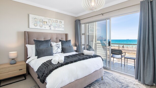 Une chambre avec un grand lit, une table de chevet, un luminaire au plafond et une vue sur la plage, accessible par une porte-fenêtre coulissante.