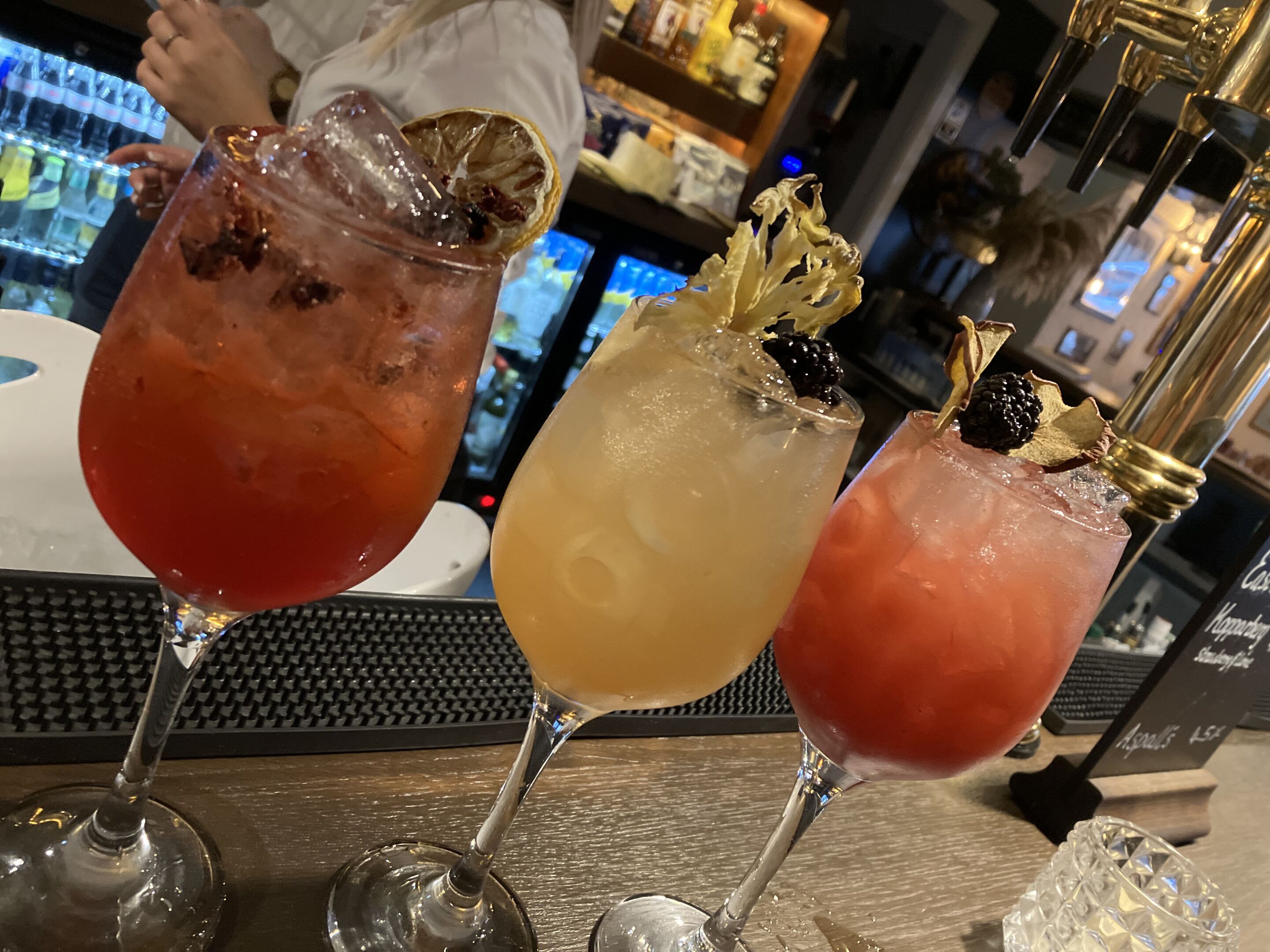 Three cocktails with garnishes on a bar counter.