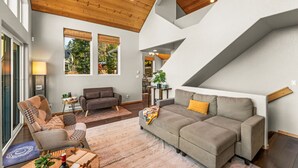 A modern living room with a high ceiling, large windows, and a staircase leading to an upper level. - Epic Views, Modern Cabin, Hot tub, Family & Pets (Woodland Park)