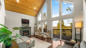 A spacious living room with a fireplace, comfortable seating, and large windows offering a view of the outdoors. - Epic Views, Modern Cabin, Hot tub, Family & Pets (Woodland Park)
