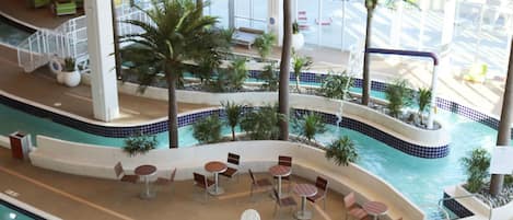 An indoor swimming pool with multiple seating areas, palm trees, and a view of the outside.