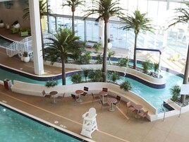 Una piscina interior con varias zonas de estar, palmeras y vistas al exterior.