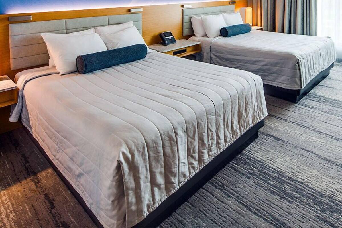 Ein Hotelzimmer mit zwei Betten, einem großen, abstrakten Wandbild und Blick ins Freie durch das Fenster.