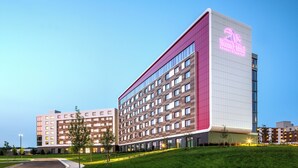 Un hôtel moderne, reconnaissable à son grand panneau néon, qui s’étend sur plusieurs étages et dispose d’un espace vert bien entretenu.