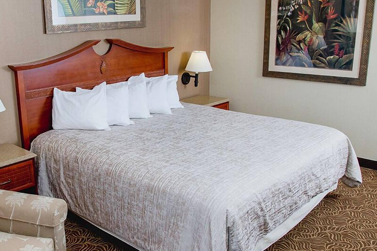Ein Hotelzimmer mit einem großen Bett, einem hölzernen Kopfteil, zwei Wandlampen, einem Sessel und zwei gerahmten Blumenbildern.
