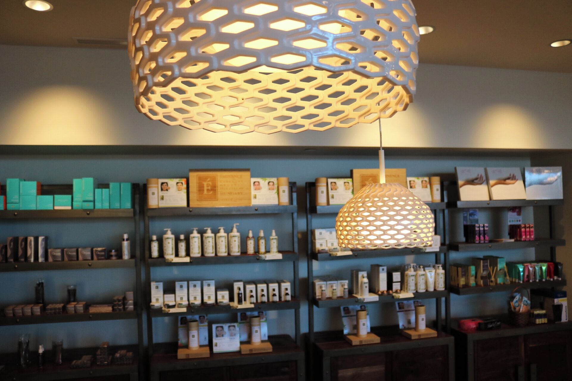 A retail store with shelves stocked with various products, a decorative hanging light fixture, and framed certificates or awards on the wall.