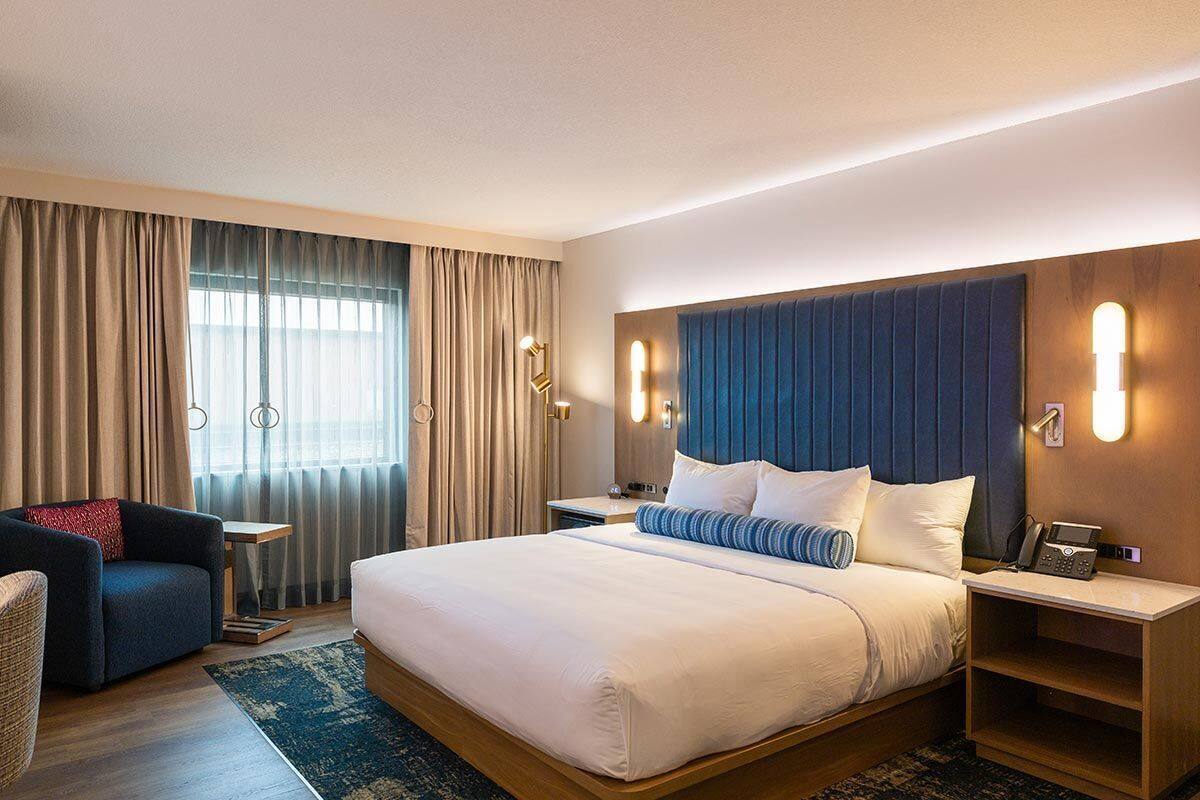 Ein Hotelzimmer mit einem großen Bett, einem Schreibtisch, einem Stuhl und Blick ins Freie durch das Fenster.