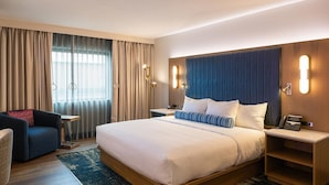 Une chambre d’hôtel avec un grand lit, un bureau, une chaise et une vue sur l’extérieur par la fenêtre.