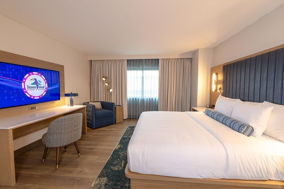 Une chambre d’hôtel avec un grand lit, un bureau avec un ordinateur, une télévision et une chaise.