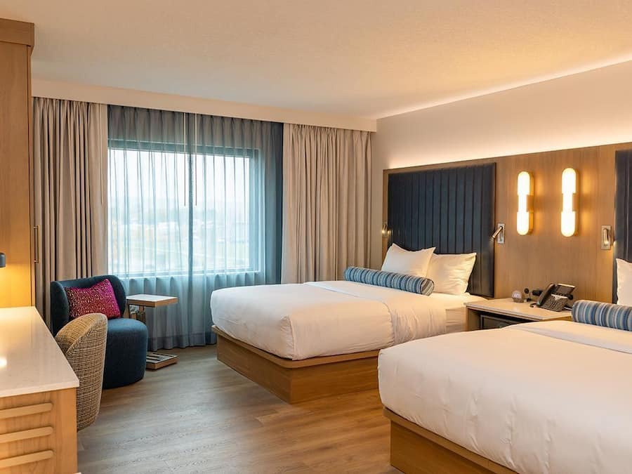 Une chambre d’hôtel avec deux lits, un bureau, une chaise et une grande fenêtre avec des rideaux.