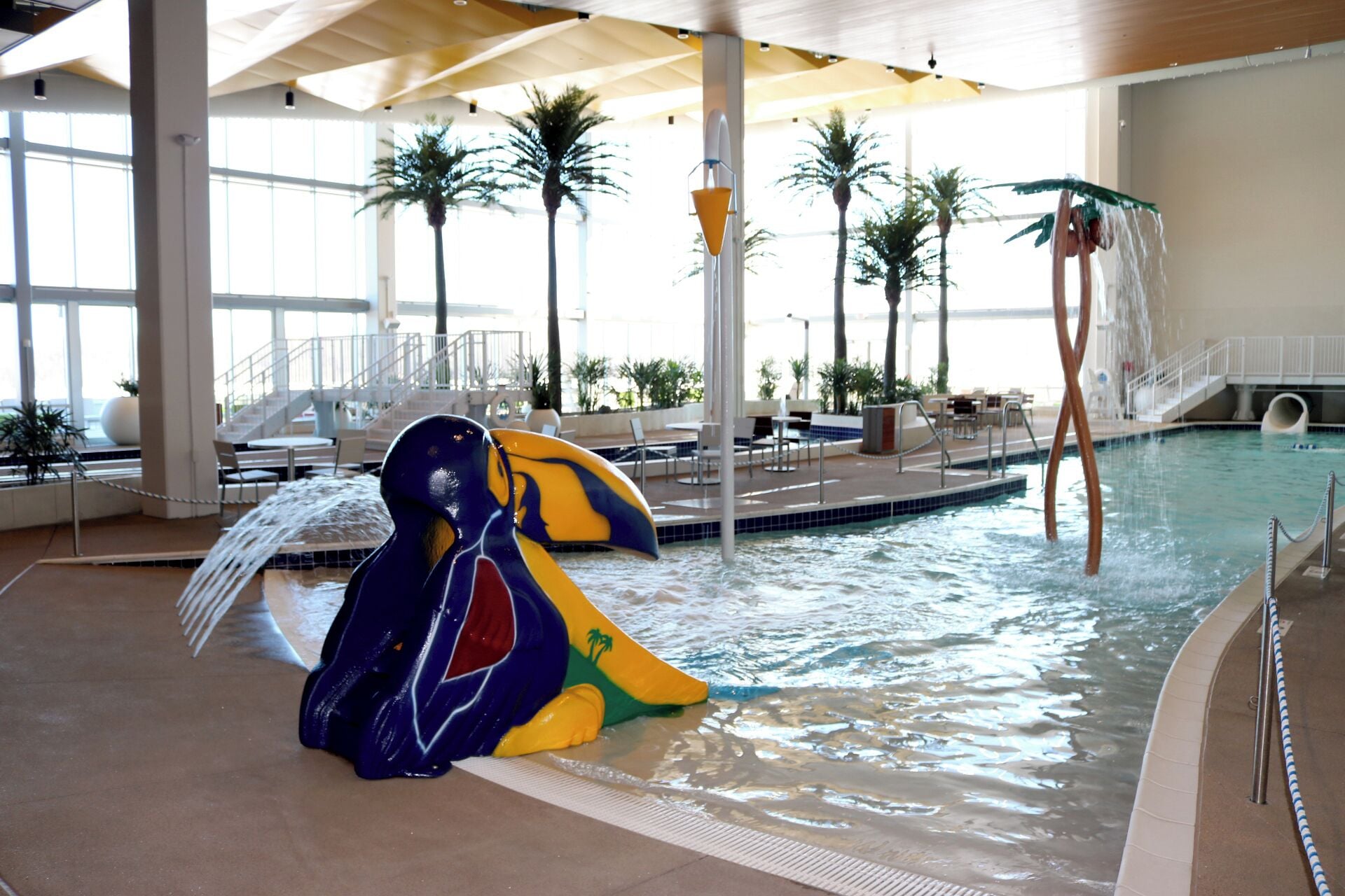 Ein Hallenbad mit Wasserrutsche, Palmen und einer überdachten Liegebereich.