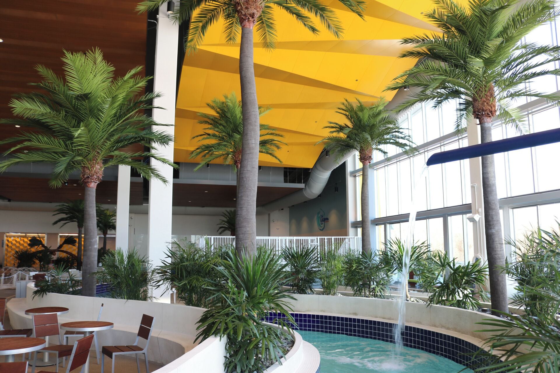An indoor pool area with palm trees, a yellow ceiling, and a tiled pool.