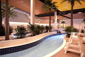An indoor swimming pool with a curved design, surrounded by palm trees and a white pool ladder. - Treasure Island Resort & Casino (Welch)