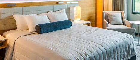 Une chambre d’hôtel avec un grand lit, une chaise, une table de chevet et une lampe.