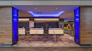 Un hall d’hôtel moderne avec un comptoir d’accueil, un kiosque d’information numérique et un sol à motifs.