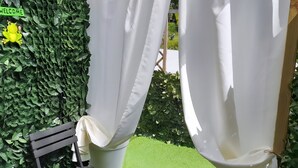 A patio area with a black wooden bench, white curtains, and a green leafy wall.