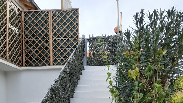 A staircase with a stone wall on one side and a metal railing on the other, leading to a building with a wooden lattice structure.