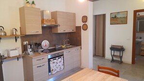 A compact kitchen with wooden cabinets, a built-in oven, and a sink. There is a dining table with chairs and a small side table with baskets.