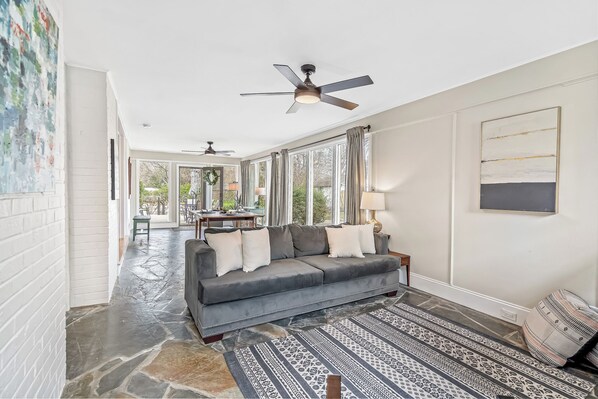 A spacious living area with a gray sofa, patterned rug, and a ceiling fan. - Relax in Historic Downtown Burlington | The Fogleman House | Minutes from Elon (Burlington)