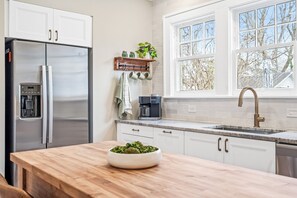 A modern kitchen with white cabinets, a stainless steel refrigerator, a coffee maker, and a window with a view of trees. - Relax in Historic Downtown Burlington | The Fogleman House | Minutes from Elon (Burlington)