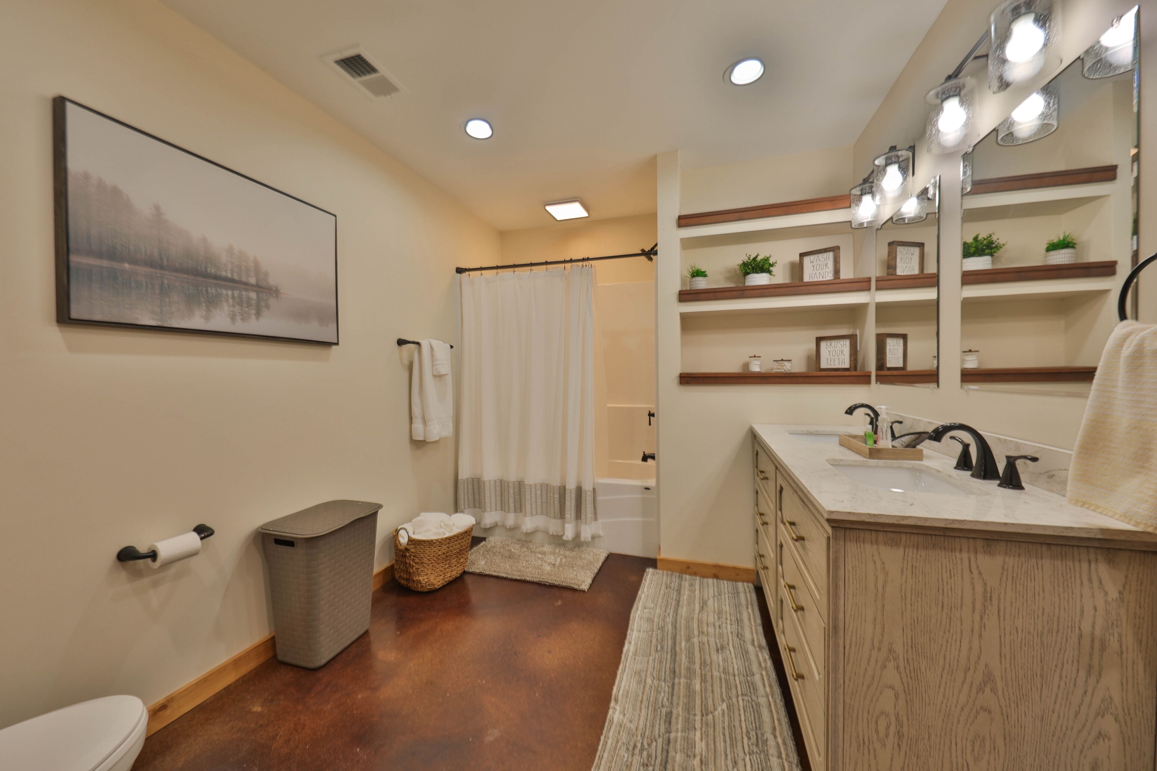 A bathroom with a wooden vanity, a large mirror, and a shelf with decorative items.