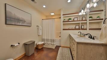 A bathroom with a wooden vanity, a large mirror, and a shelf with decorative items.