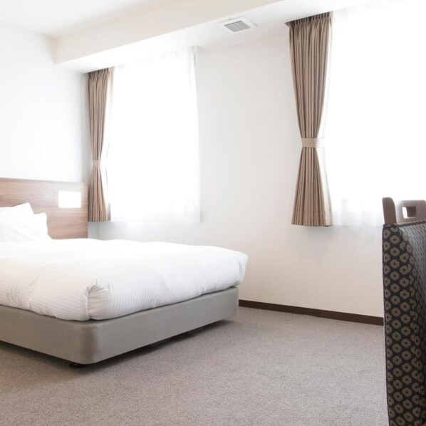 A hotel room with a bed, curtains, a headboard, and a patterned armchair.