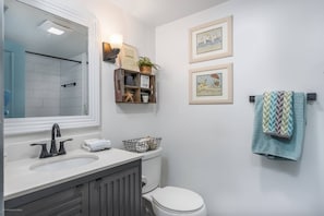A bathroom with a white sink, a toilet, and a towel rack with a towel. There are framed pictures on the wall and a shelf with decorative items.