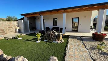 A modern house with a covered patio, stone walls, and a well-maintained lawn.