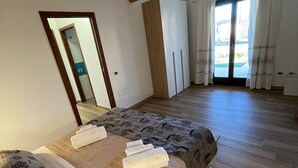 Une chambre avec un plafond en bois, un grand lit avec une literie à motifs, un tapis blanc et une vue à travers une porte.