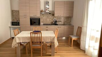 A compact kitchen with wooden cabinets, a microwave, a stove, and a dining area with a table and chairs.