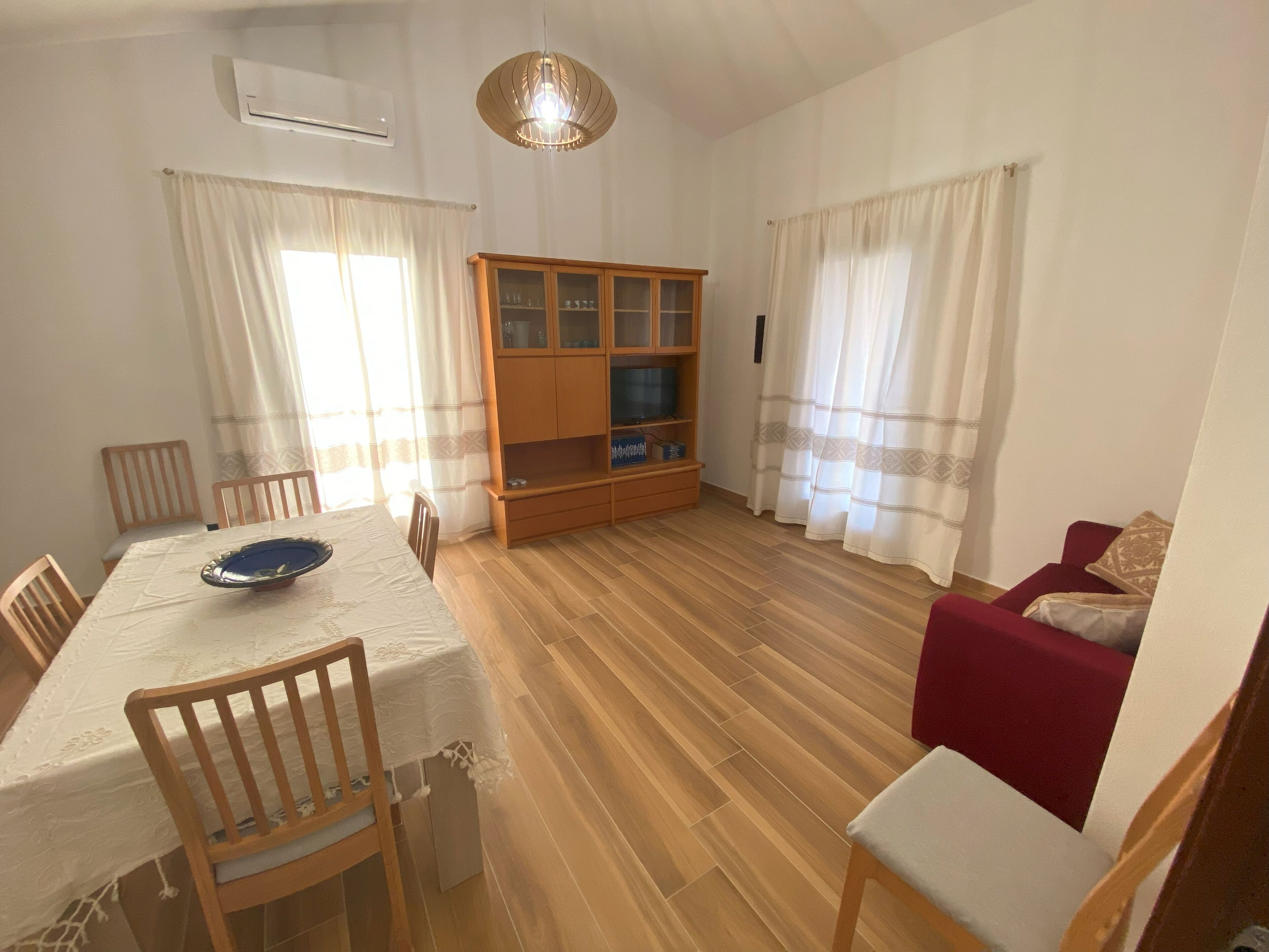A dining area with a table, chairs, a wooden cabinet, and a red sofa.