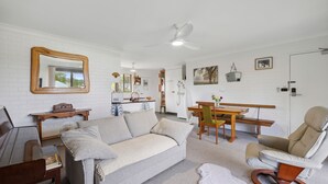 A living room with a sofa, a chair, a dining table, and a ceiling fan.