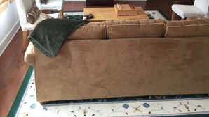 Ein Wohnzimmer mit beiger Couch, einem Flachbildfernseher, einem Gemälde an der Wand und einem Deckenventilator.