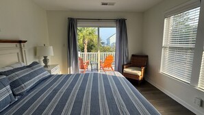 A bedroom with a bed, a chair, a lamp, and a balcony with chairs. - “Crescent Moon” - 5BR – established, top rated, dog friendly, 5 min walk to beach! (Folly Beach)