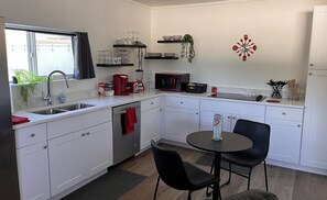 A modern kitchen with white cabinets, a black countertop, a microwave, and a dining area with two chairs.