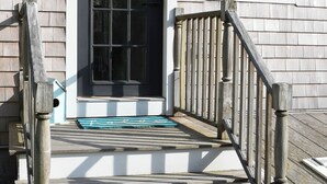 Eine Holztreppe führt zu einer weißen Tür mit einem schwarzen Fenster darüber.