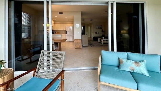 A modern living room with a blue sofa and a wicker chair, a sliding glass door leading to a kitchen and dining area. - Beautiful Relaxing condo with a Lake/Golf Course view 8 miles from beach! (Fort Myers)