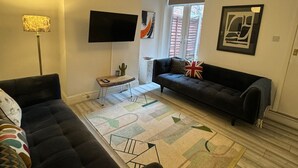 Una sala de estar moderna con un sofá negro, un tapete estampado, una lámpara de pie y obras de arte en las paredes.