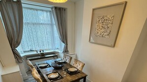 Comedor con mesa de madera para cuatro, lámpara colgante y ventana con cortinas.