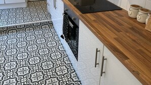 Cocina moderna con armarios blancos, encimera de madera, horno integrado y baldosas de suelo estampadas.